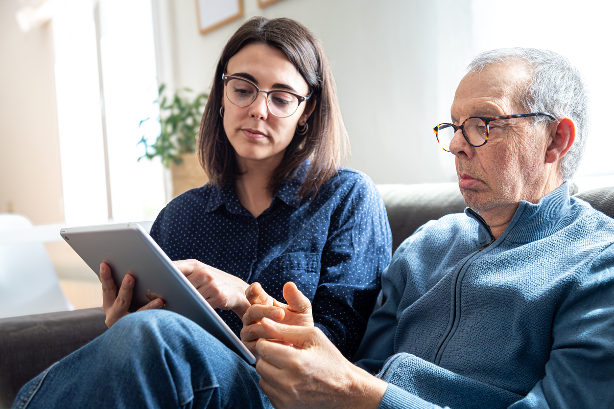 Adult daughter sitting with father, helping him on a tablet