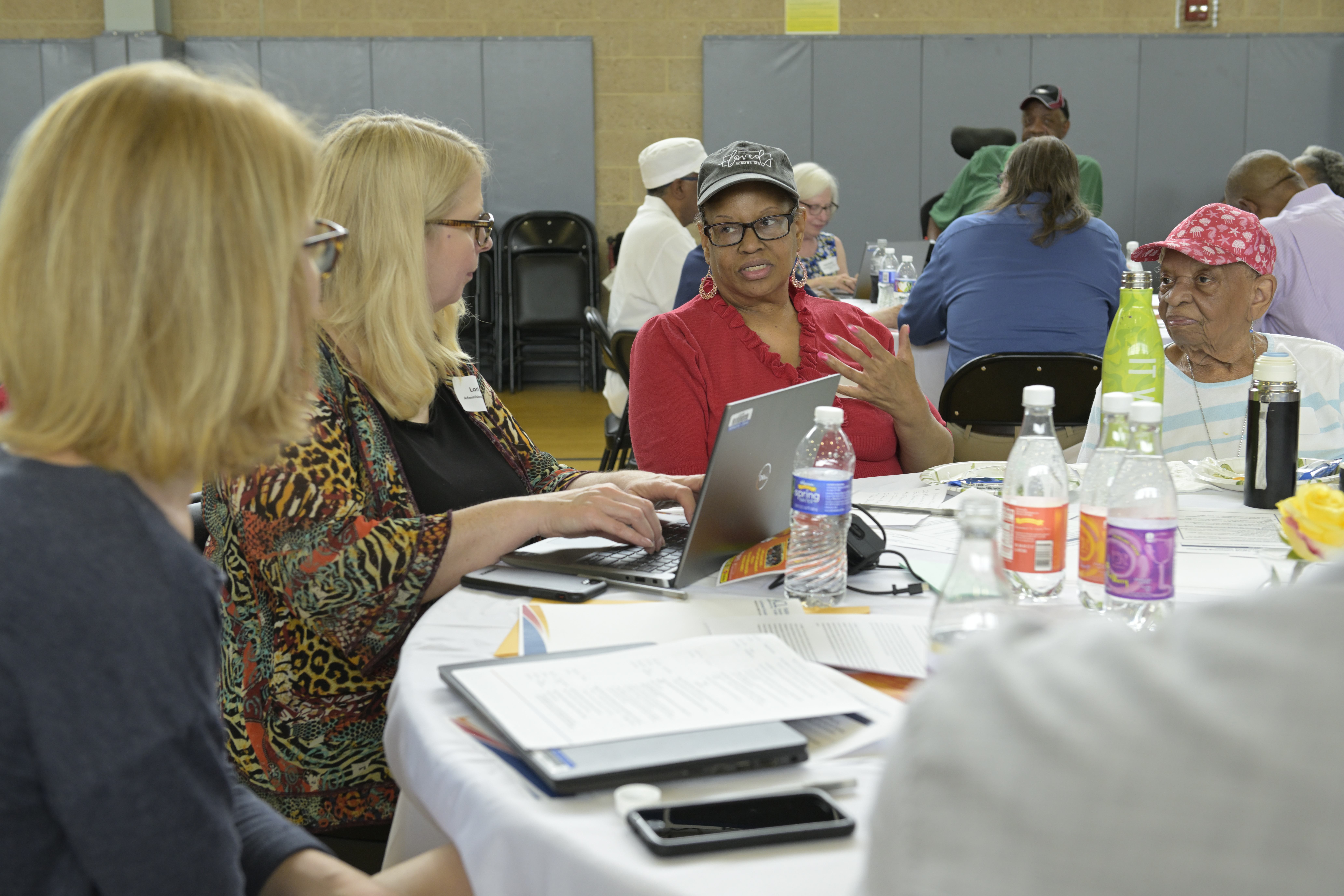 Adults participating in a group discussion around a table with a laptop and printed materials.