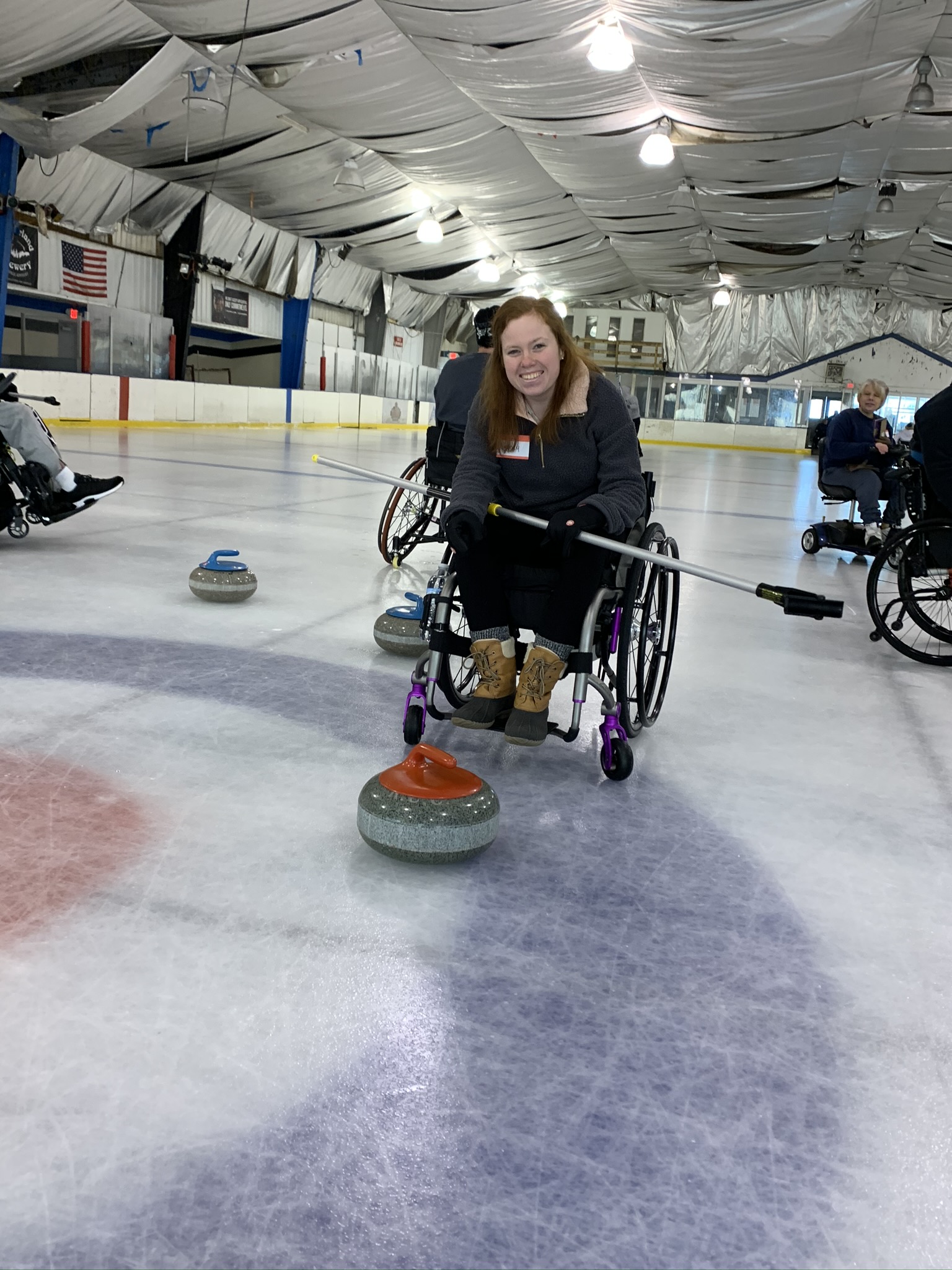 Smiling woman in wheelchair on ice with curling stone