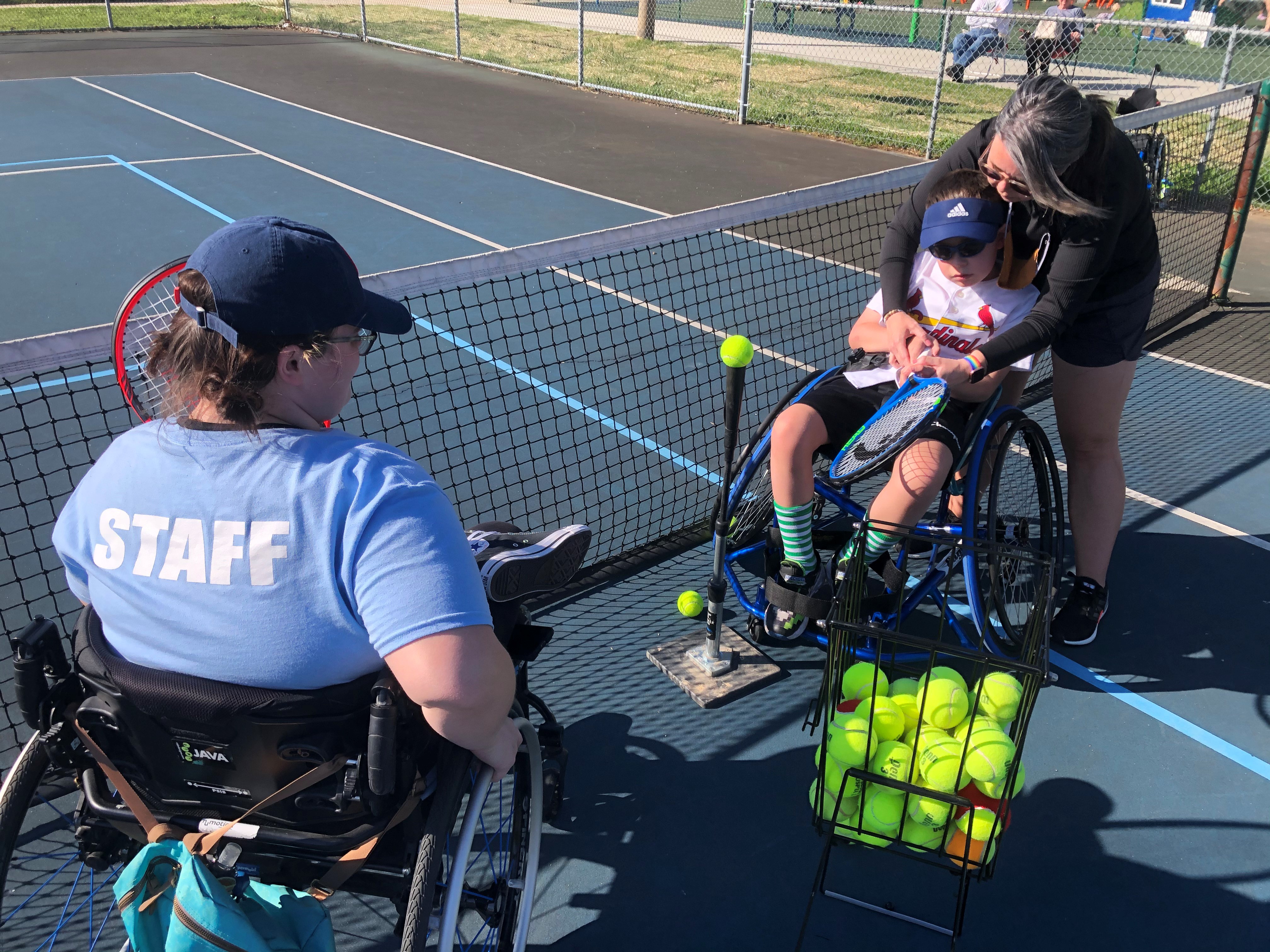Woman in wheelchair teaching tennis to boy in wheelchair