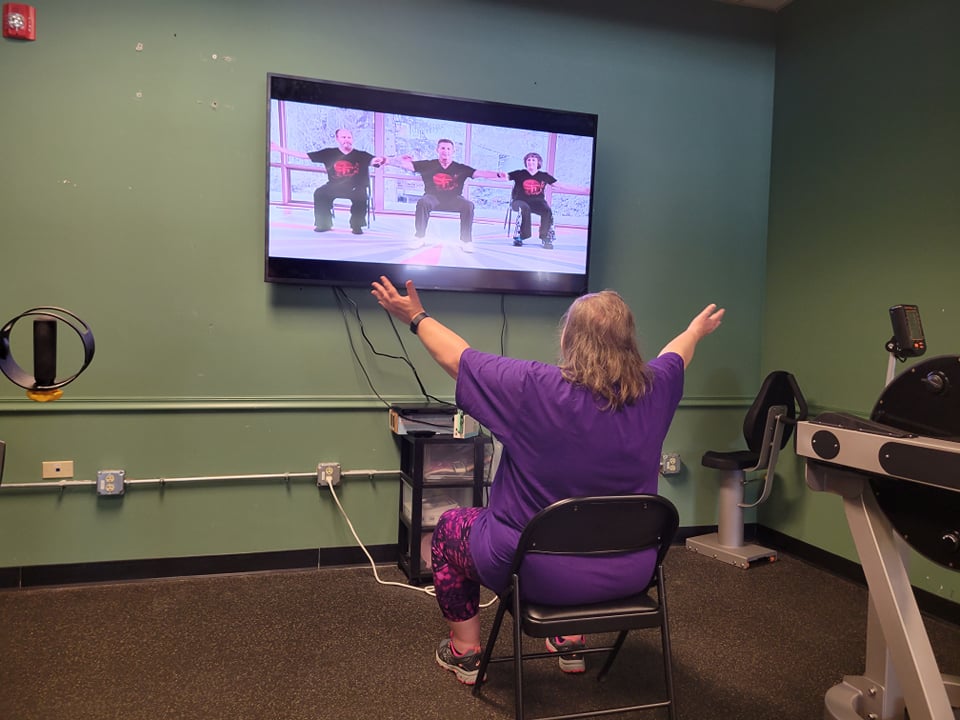 Program participant exercises while seated in a chair following a video workout