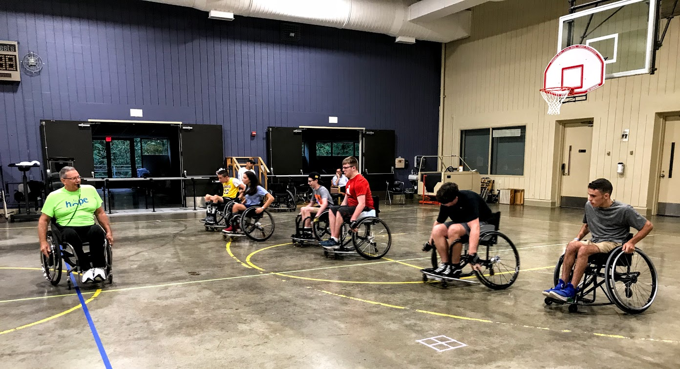 A coach gives instruction as wheelchair basketball players start moving toward him on the court