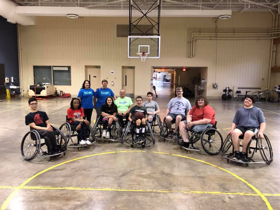 A group of people in the wheelchair basketball program sit together on the court