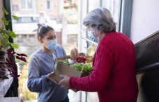 Young woman wearing face mask handing box of food to older woman wearing face mask
