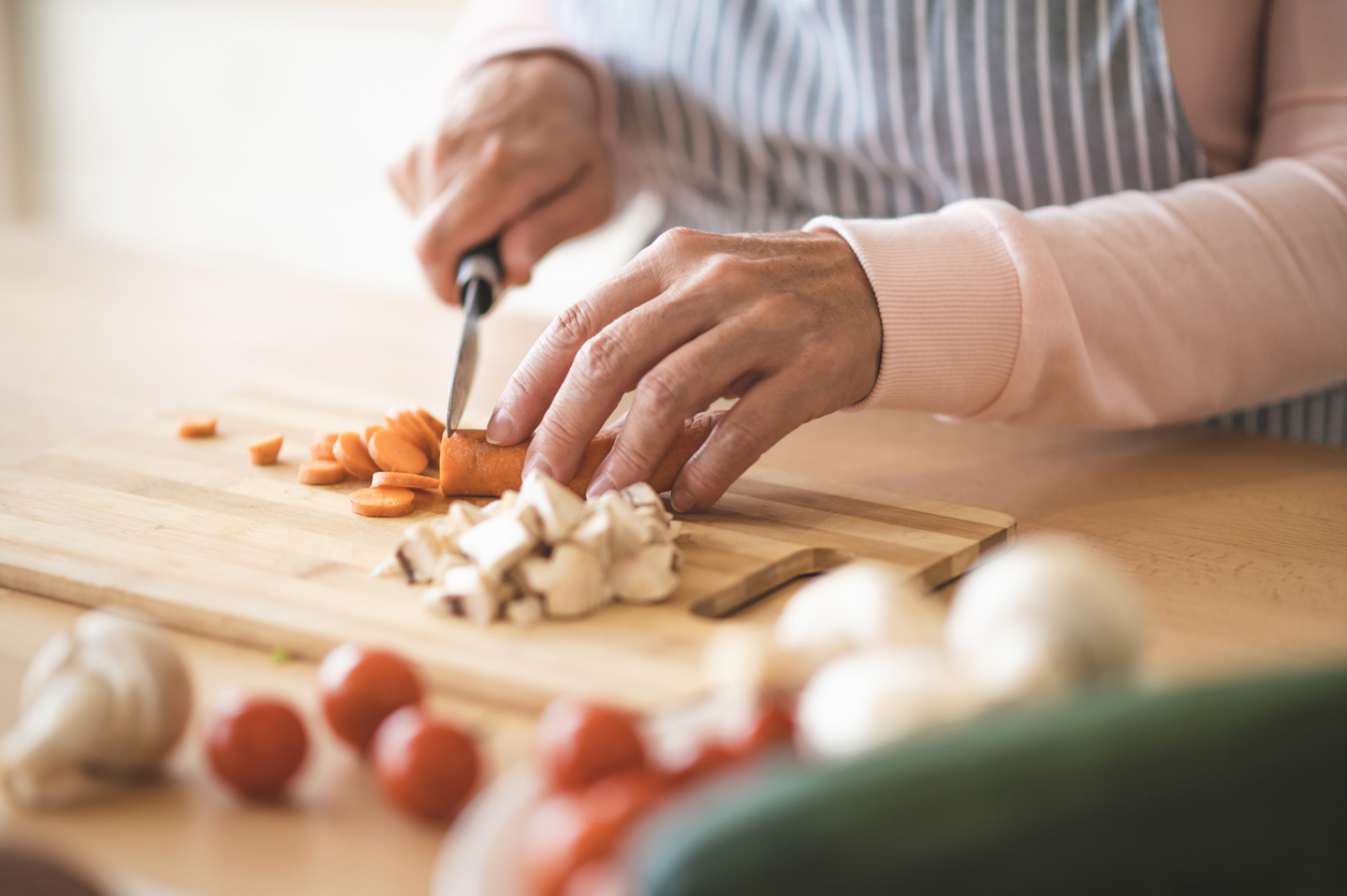 Close-up photo of the hands of an older woman chopping vegetables