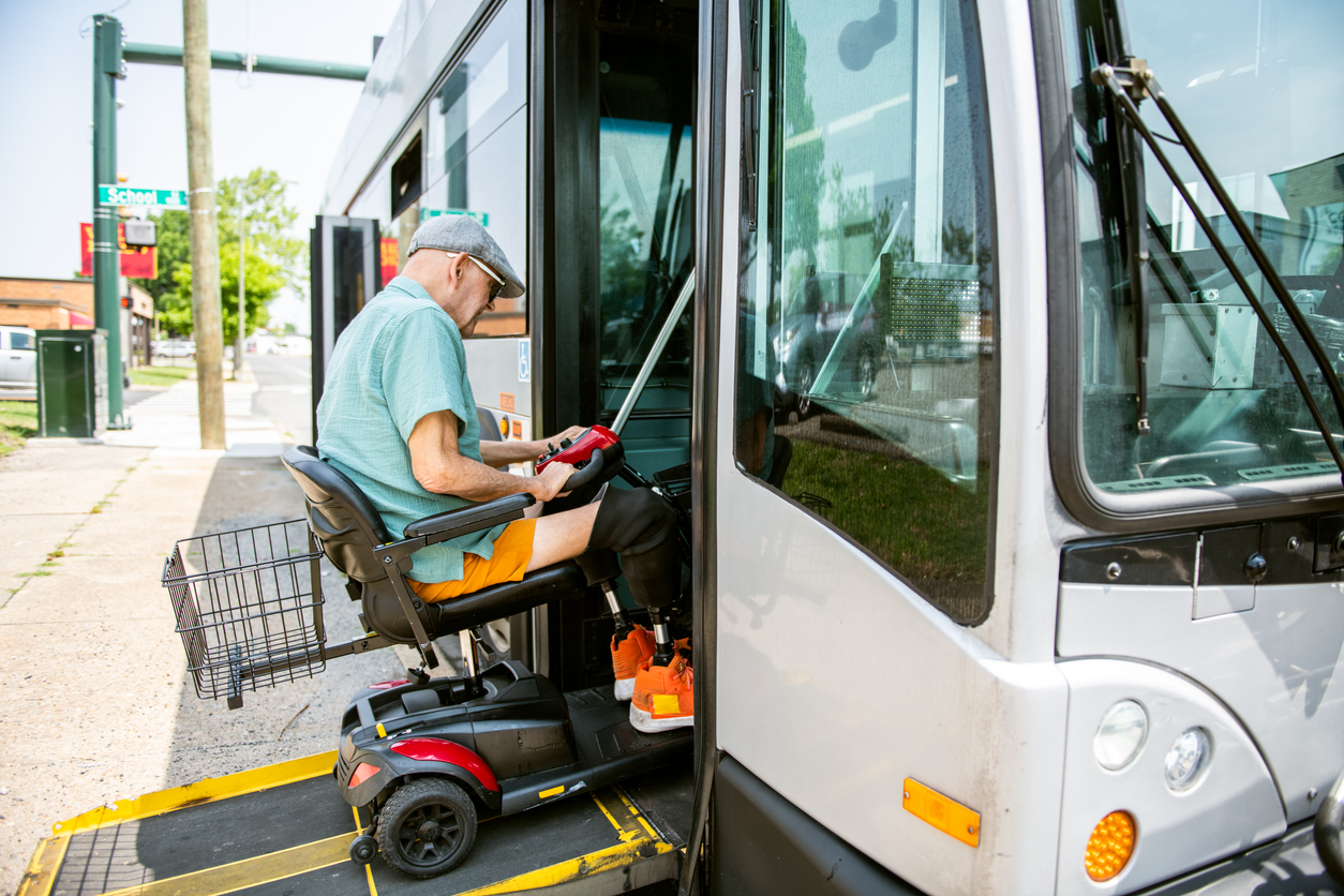 Older man boards bus on his motorized scooter
